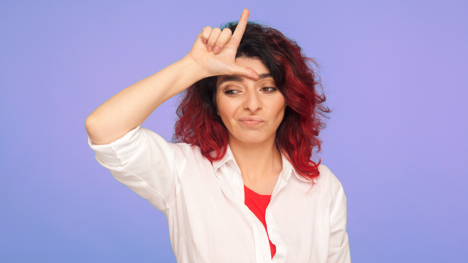 A feminine person with red hair makes an L (as in "loser") sign on their forehead